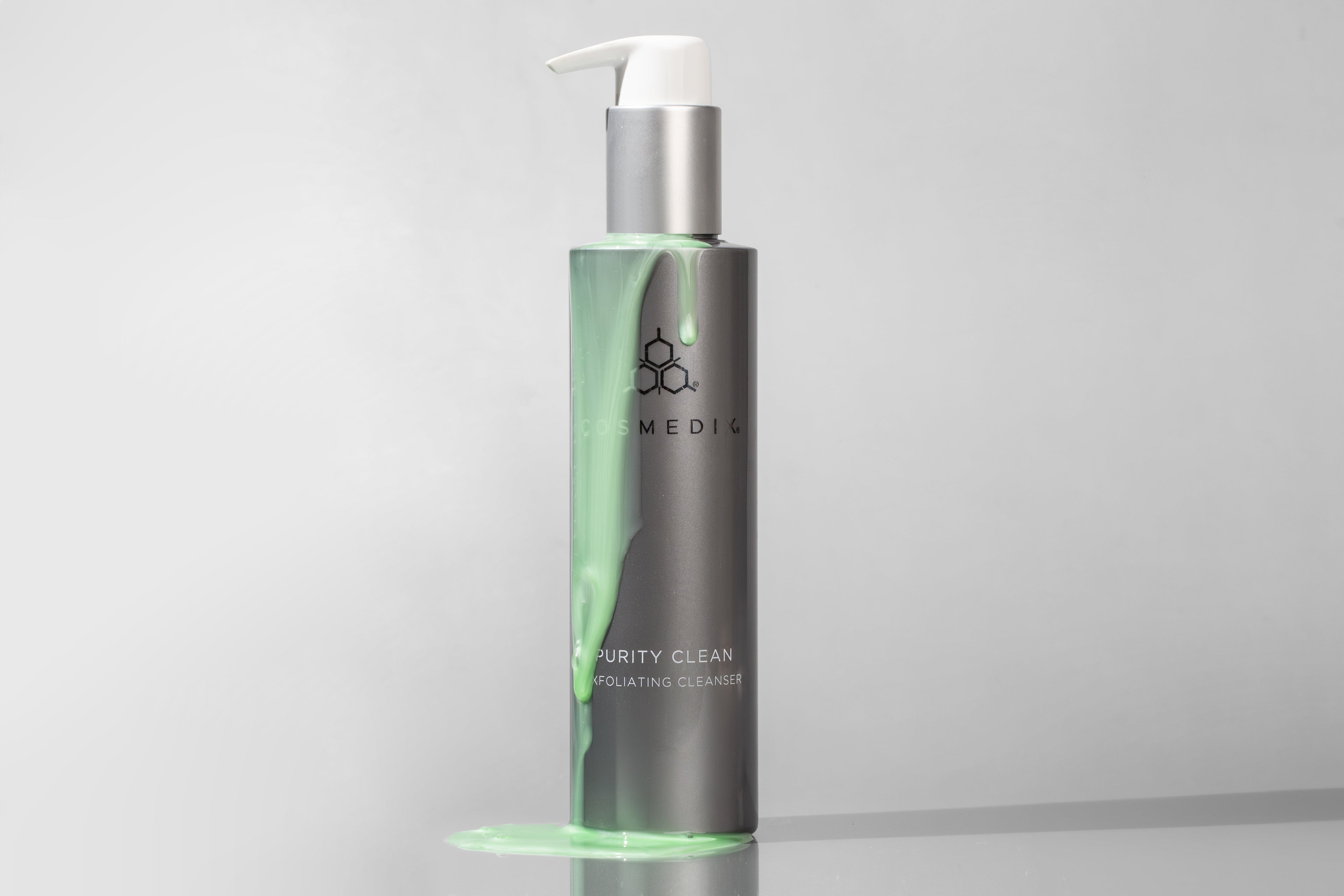 Cosmedix Purity Clean Cleanser with the green cleanser dripping on the bottle with a grey background