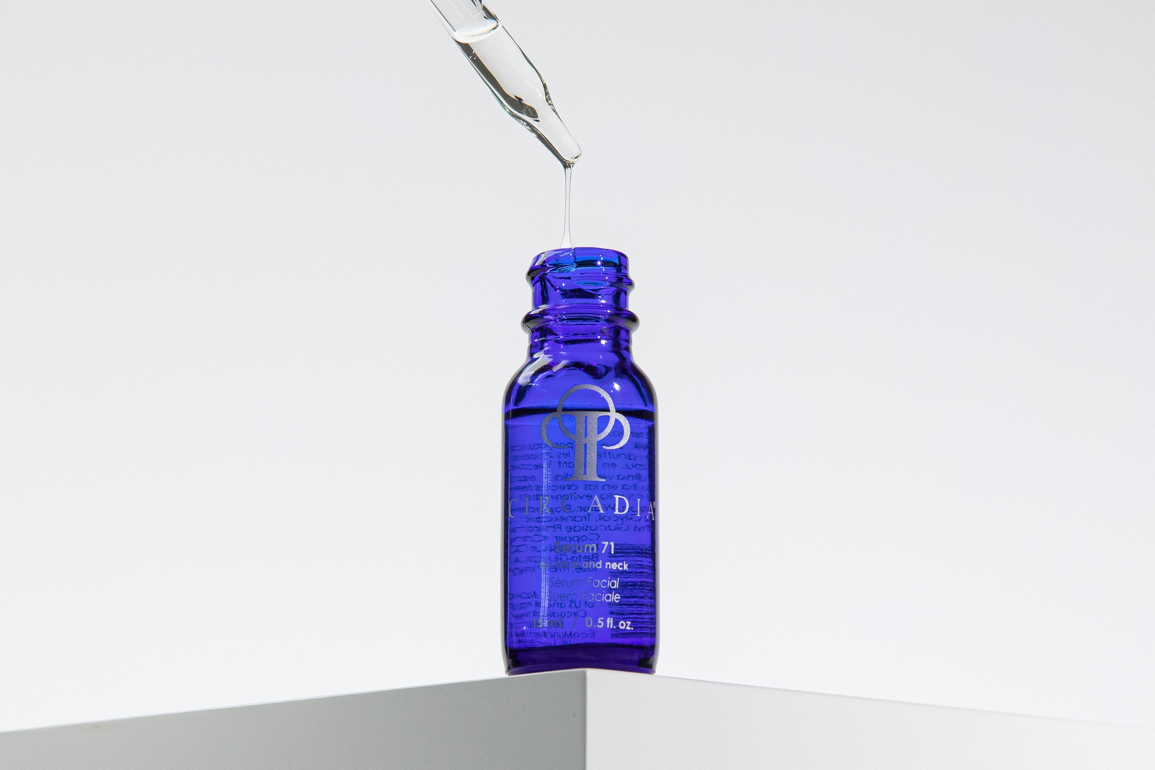 Circadia Serum 71 bottle sitting on a white platform edge with a serum dropper over it on a white background