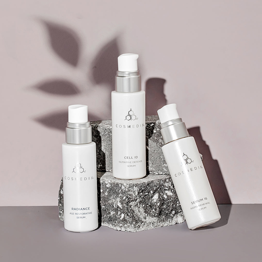 Cosmedix serums sitting on a rock with a leaf shadow and a grey background