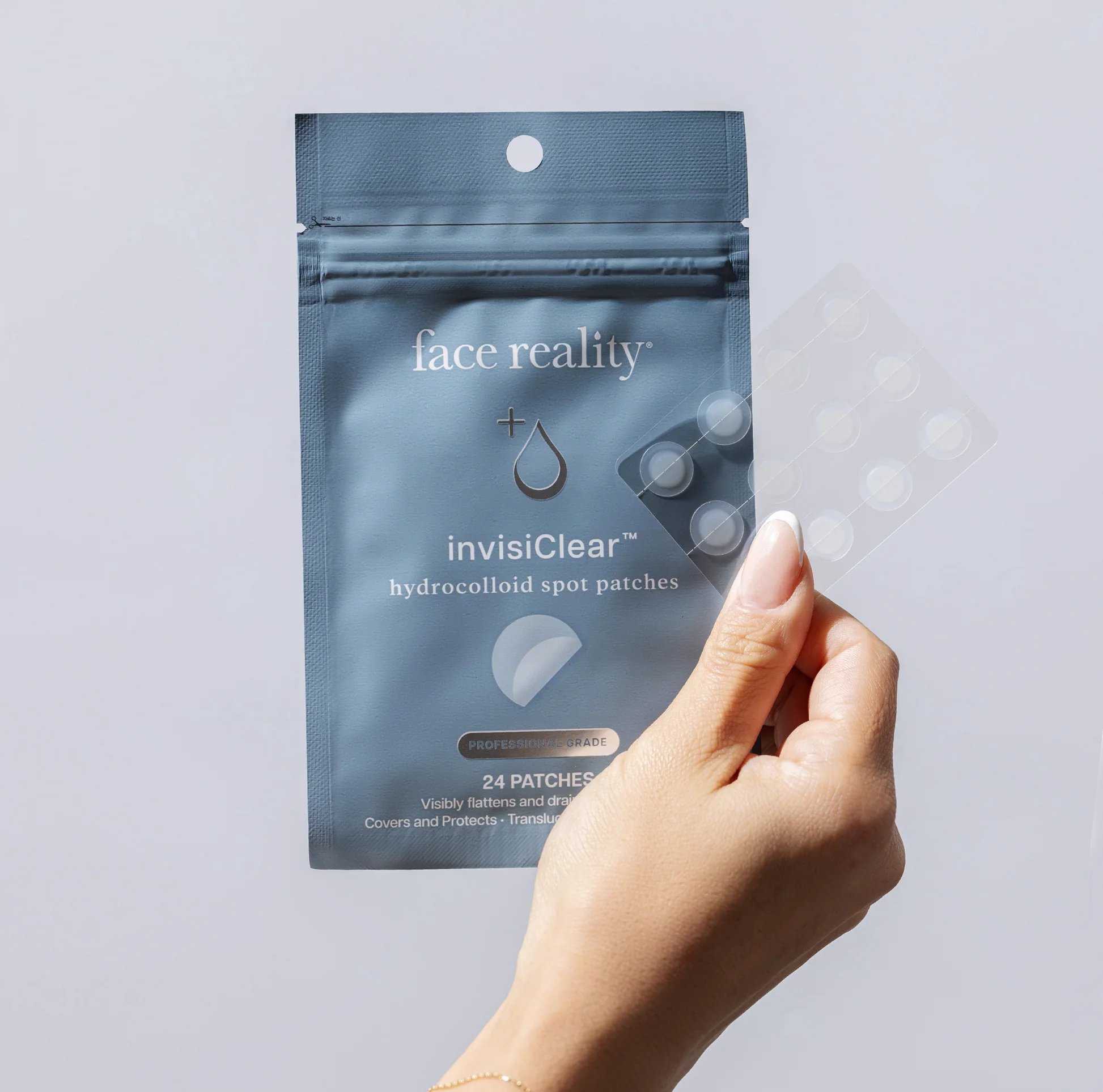 Hand holding a package of Face Reality invisiClear hydrocolloid spot patches against a light gray background
