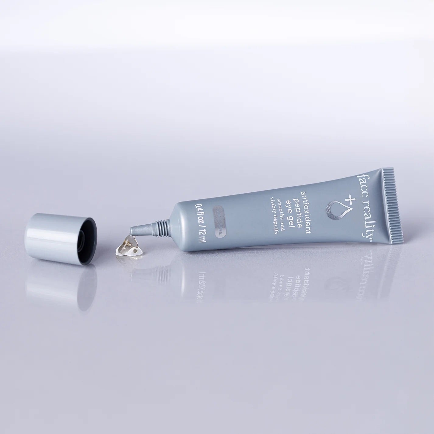 Face Reality's antioxidant peptide eye gel blue tube laying on side with cap off and product coming out, on a blue backdrop.