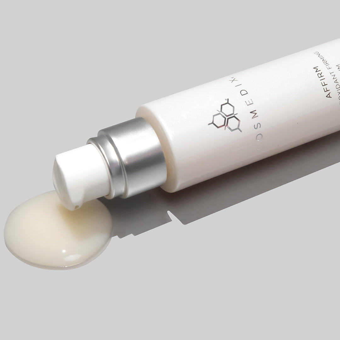 COSMEDIX's Affirm Antioxidant Firming Serum product bottle laying on side with cream-colored product swatch dispensed, against light grey background
