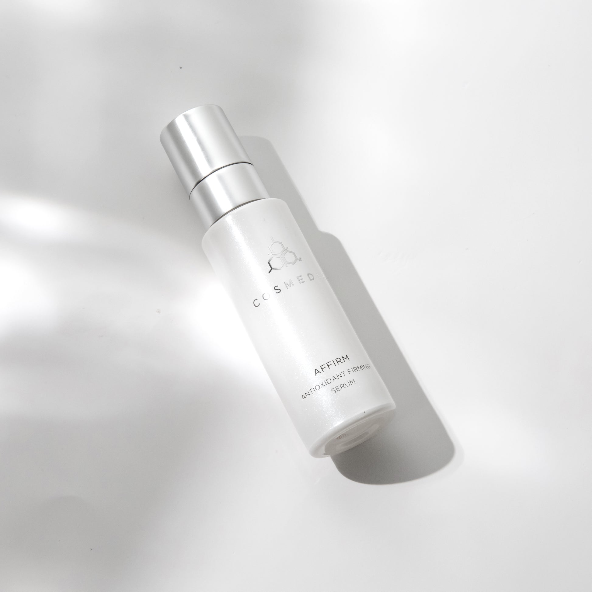 COSMEDIX's Affirm Antioxidant Firming Serum white product bottle laying on white and grey background
