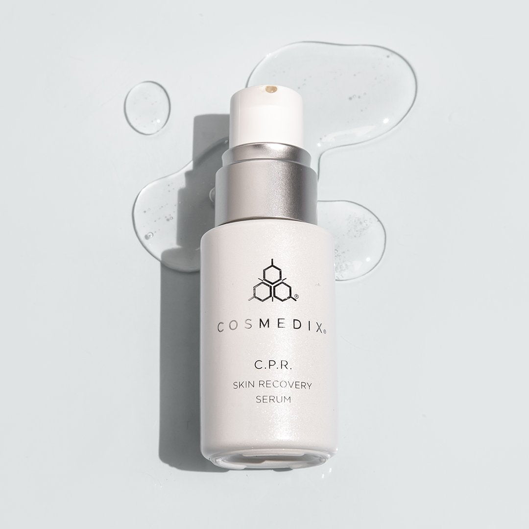 COSMEDIX's C.P.R Skin Recovery Serum white product bottle with pump dispenser laying on top of clear colored product swatch with a grey background