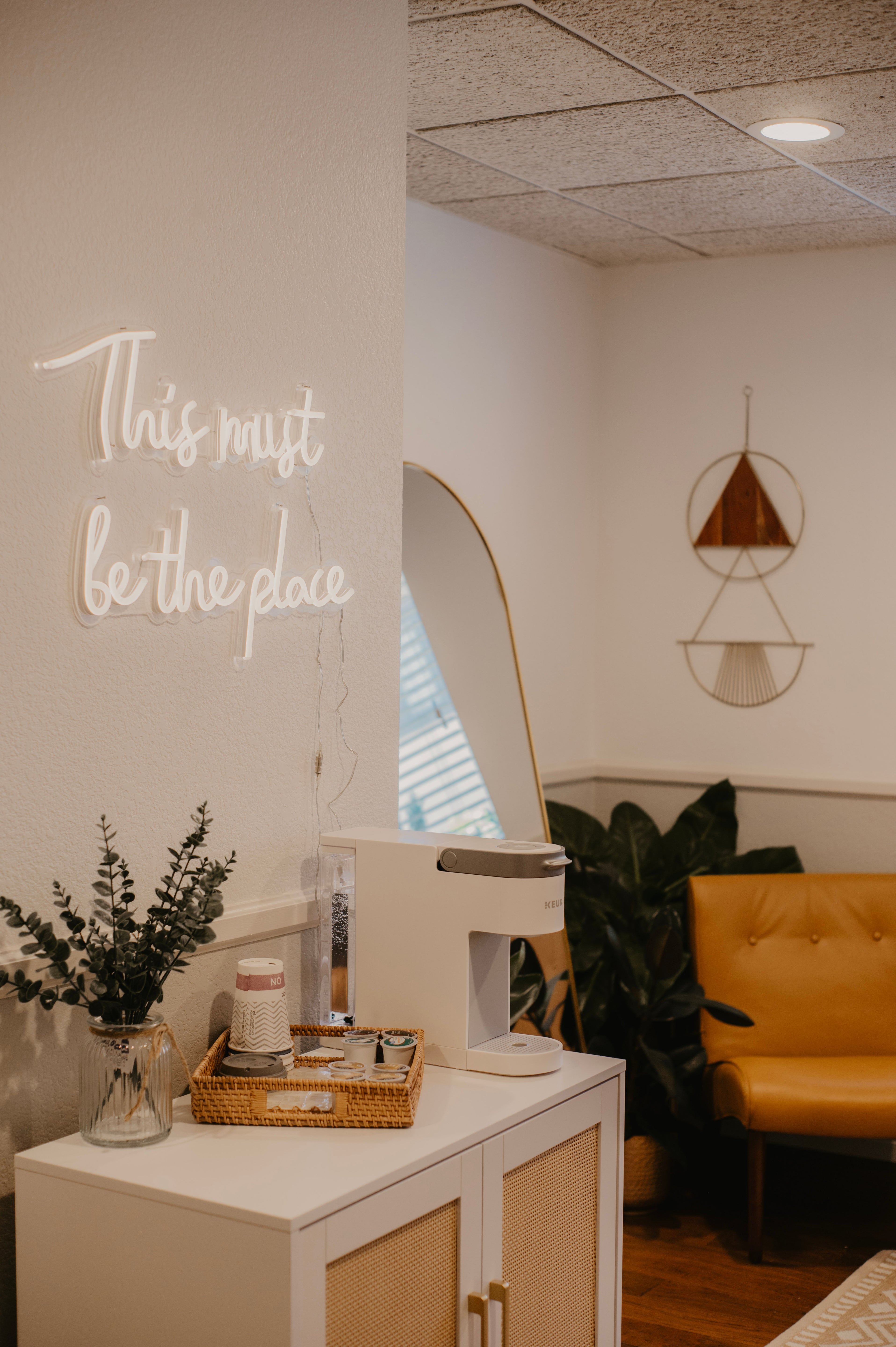 Neon sign on a wall with a modern interior setting featuring a yellow chair and decorative plants.