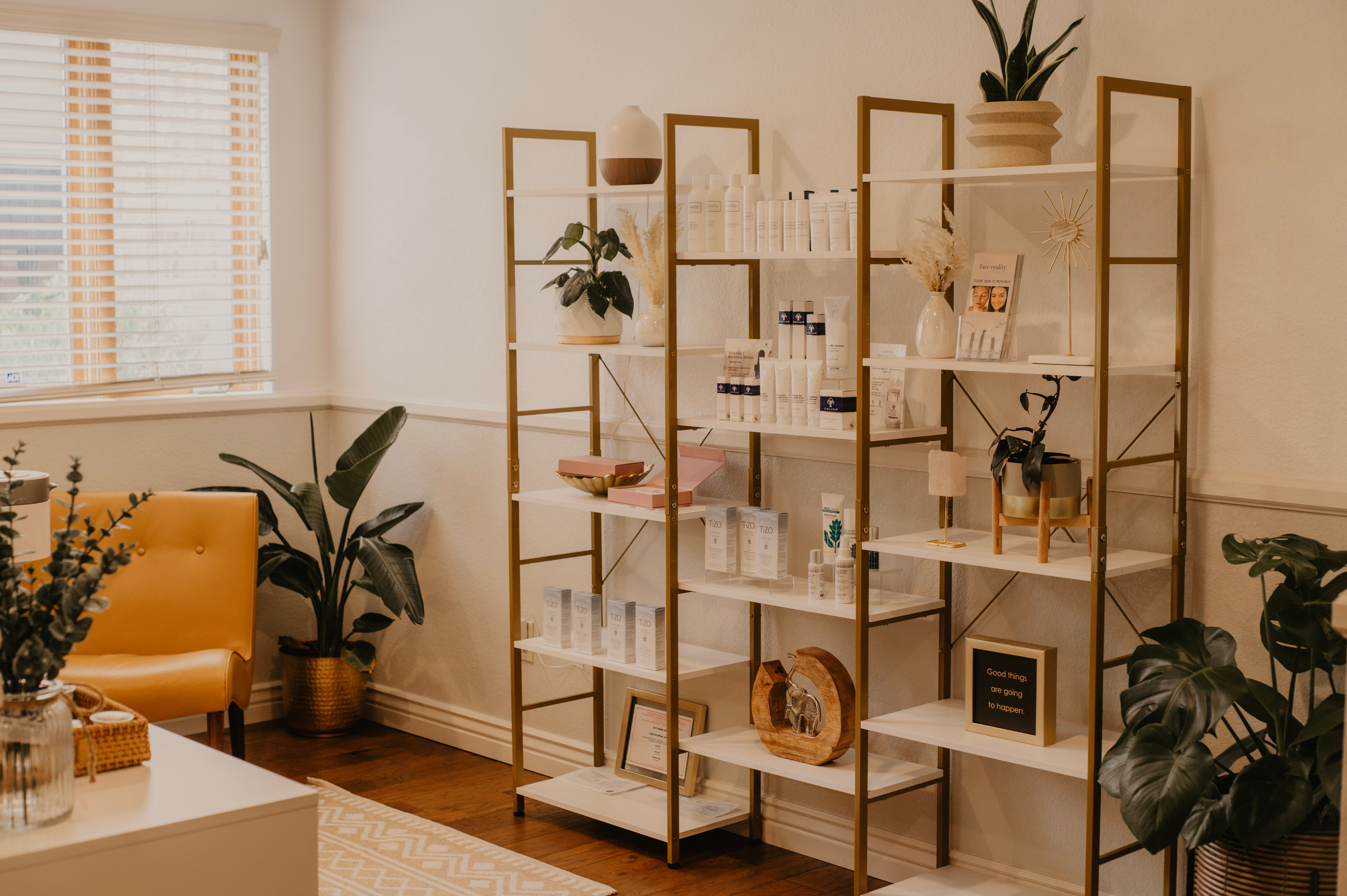 Luna Luxe Aesthetics spa interior with a bookshelf with decorations and skincare products, yellow chair, and plants in Colorado Springs