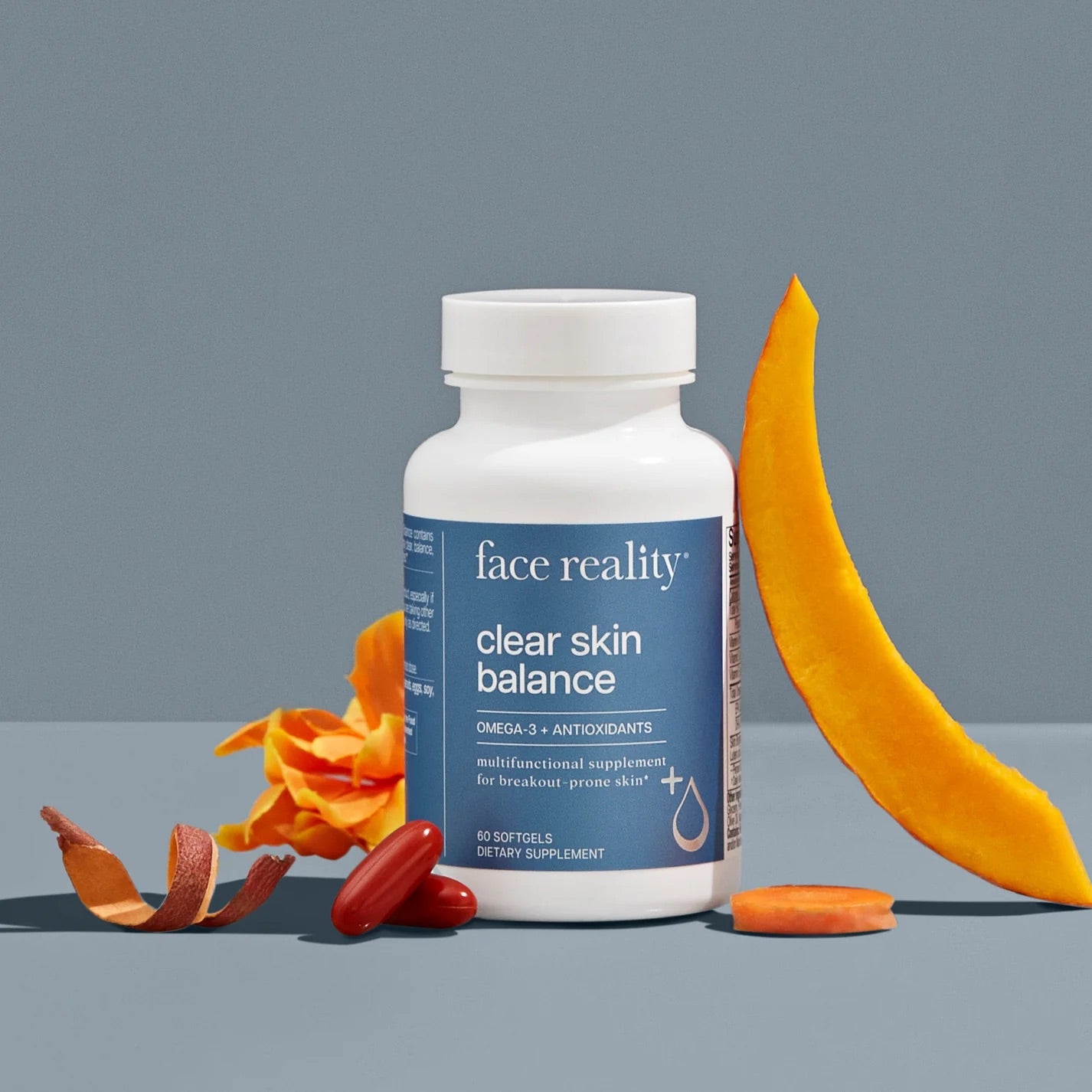 Face Reality's clear skin balance product bottle with orange fruit and orange product capsules in front of the bottle. On blue backdrop.