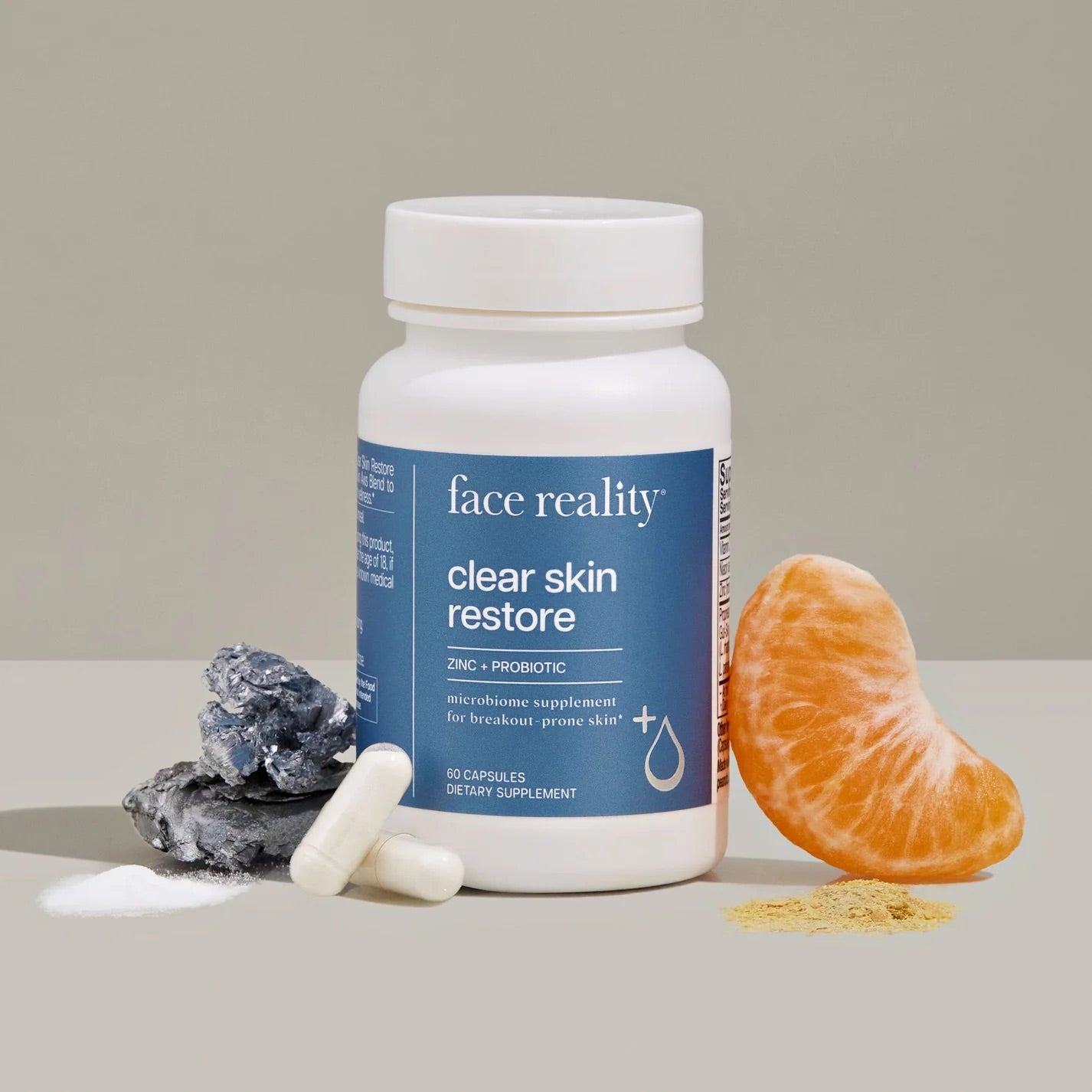 Face Reality's clear skin restore product bottle with orange fruit and white product capsules in front of the bottle. On beige backdrop.