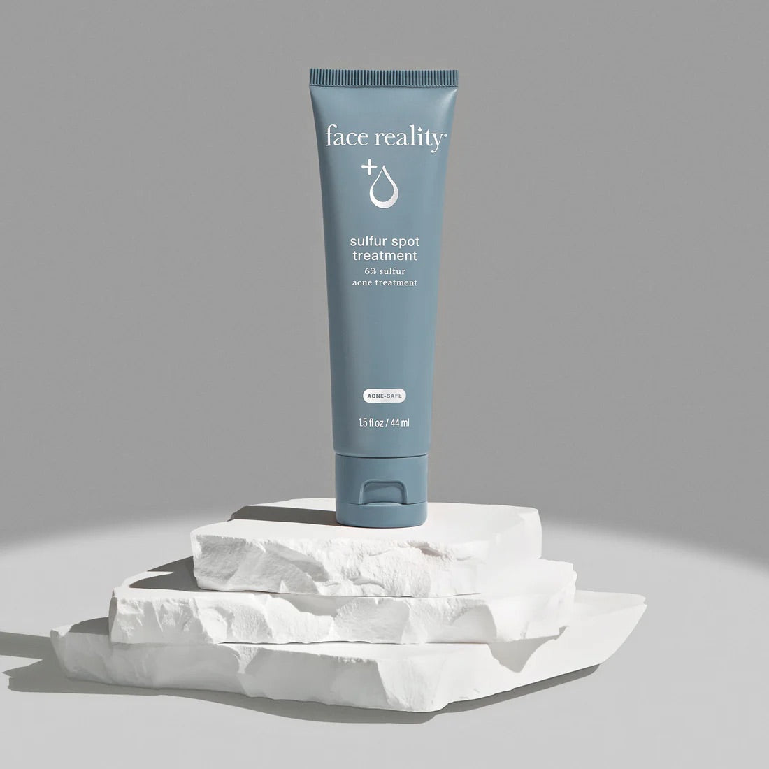 Face Reality's sulfur spot treatment blue product tube standing on white stone against grey background