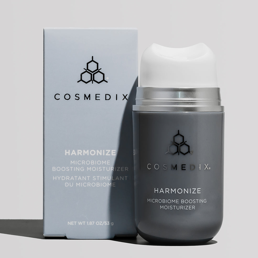 COSMEDIX's Harmonize Microbiome Boosting Moisturizer in dark grey product bottle with white pump dispenser, standing beside blue/grey product packaging box against a light grey background