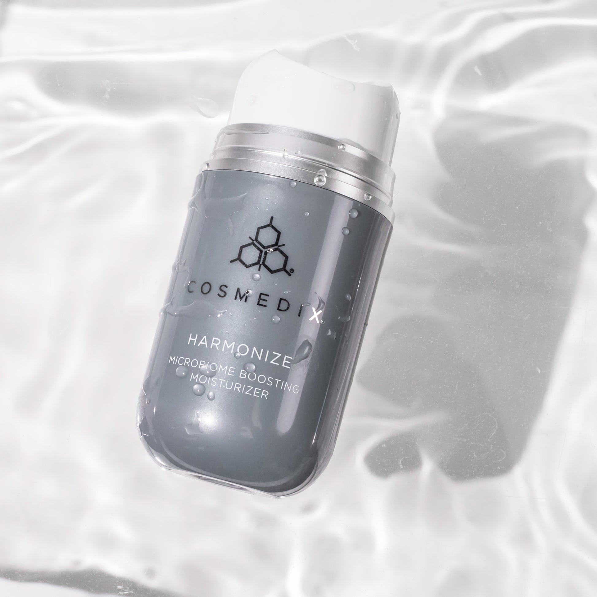 COSMEDIX's Harmonize Microbiome Boosting Moisturizer in a dark grey product bottle with white dispenser floating in water