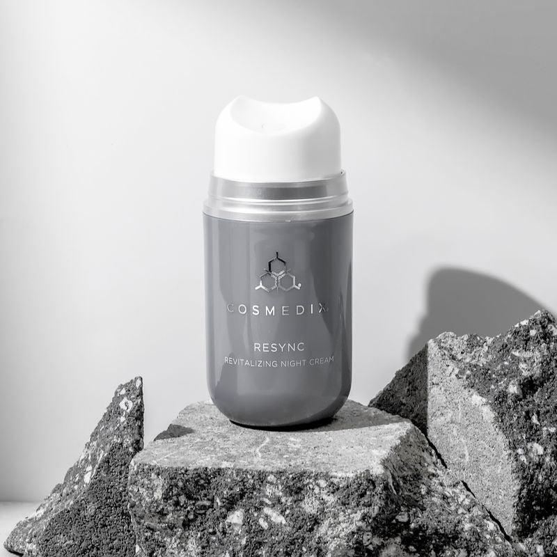 COSMEDX's Resync Revitalizing Night Cream grey product bottle with white dispenser standing on granite against light grey background