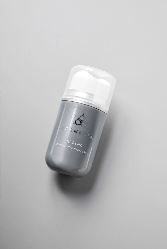 COSMEDX's Resync Revitalizing Night Cream grey colored product bottle with white top laying against light grey background