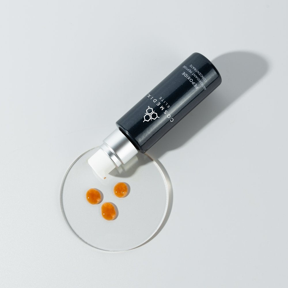 COSMEDIX's Pepoxide Antioxidant Peptide Concentrate black colored product bottle laying on side, with orange colored product swatches on petri dish against light grey background