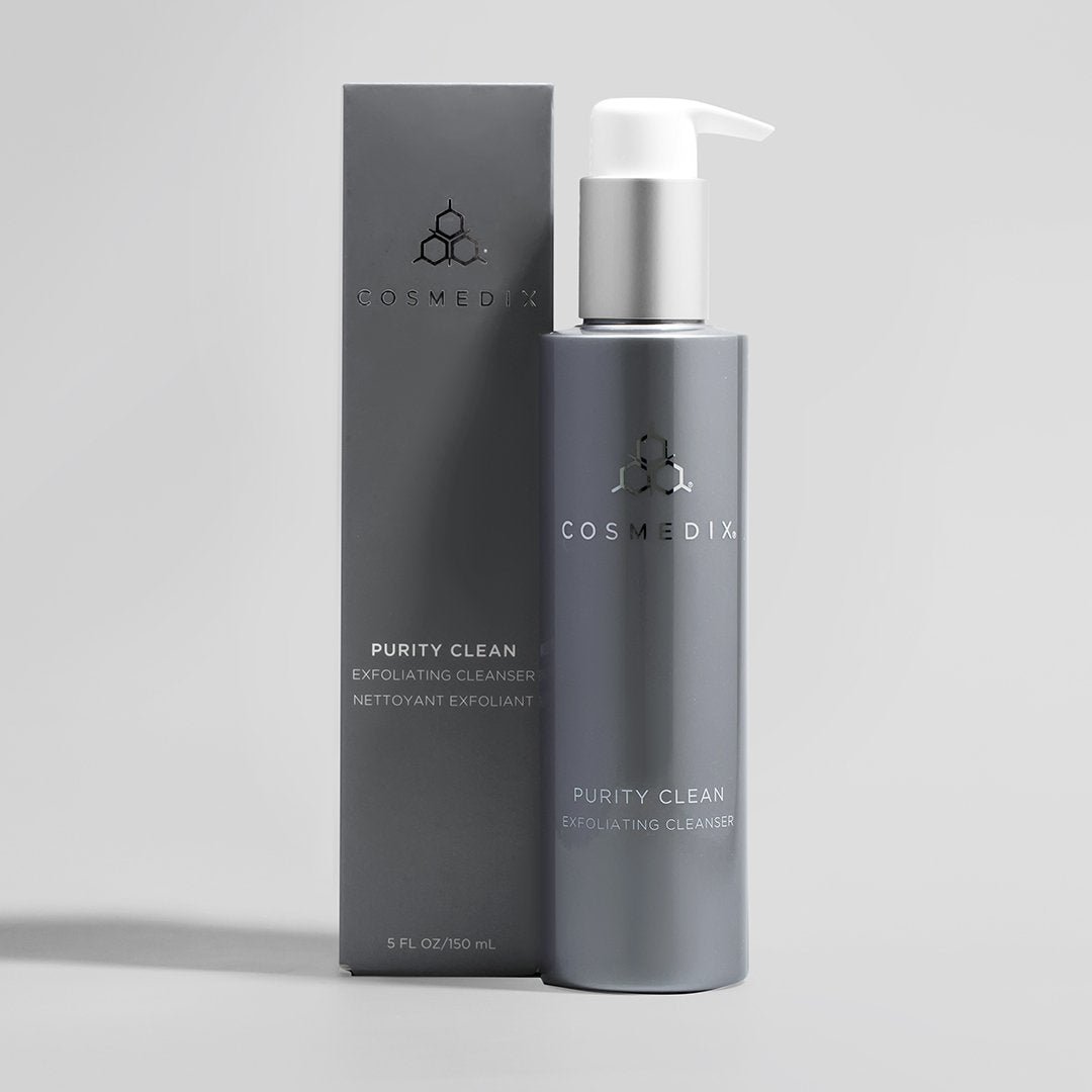 COSMEDIX's Purity Clean Exfoliating Cleanser grey product bottle with white dispenser standing beside dark grey product box against a light grey background