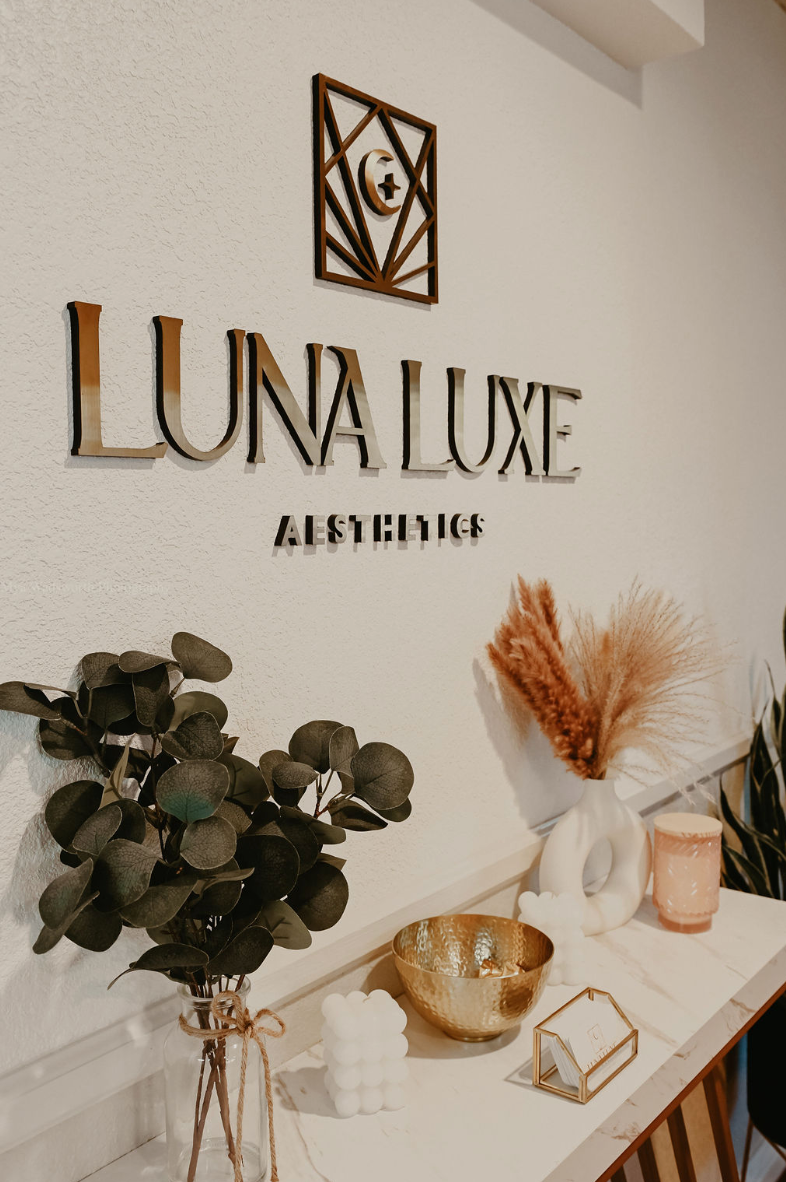 Luna Luxe Aesthetics logo on a wall with decorative items on a table below.