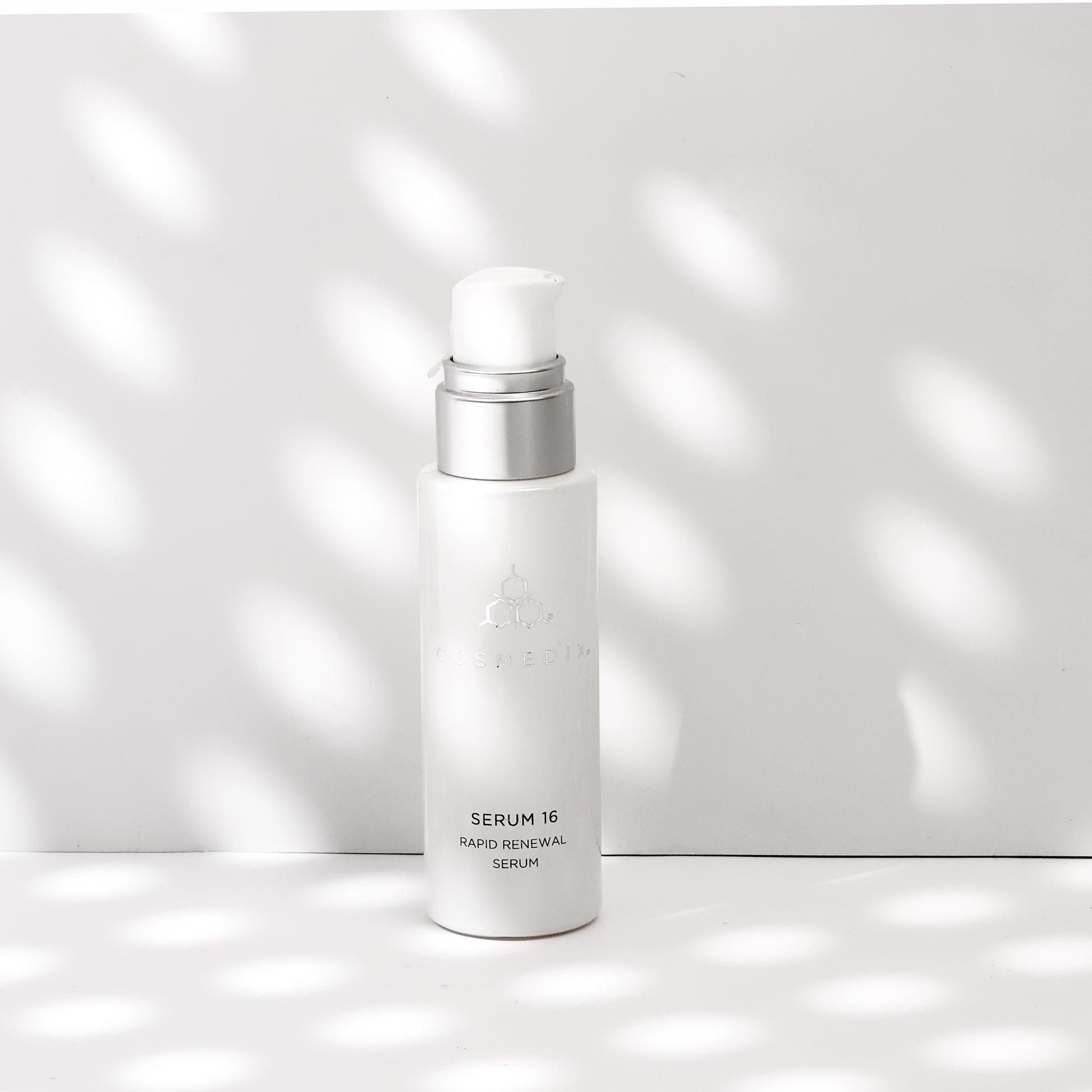 COSMEDIX's Serum 16 Rapid Renewal Serum white product bottle with dispenser, standing against white and grey shadows