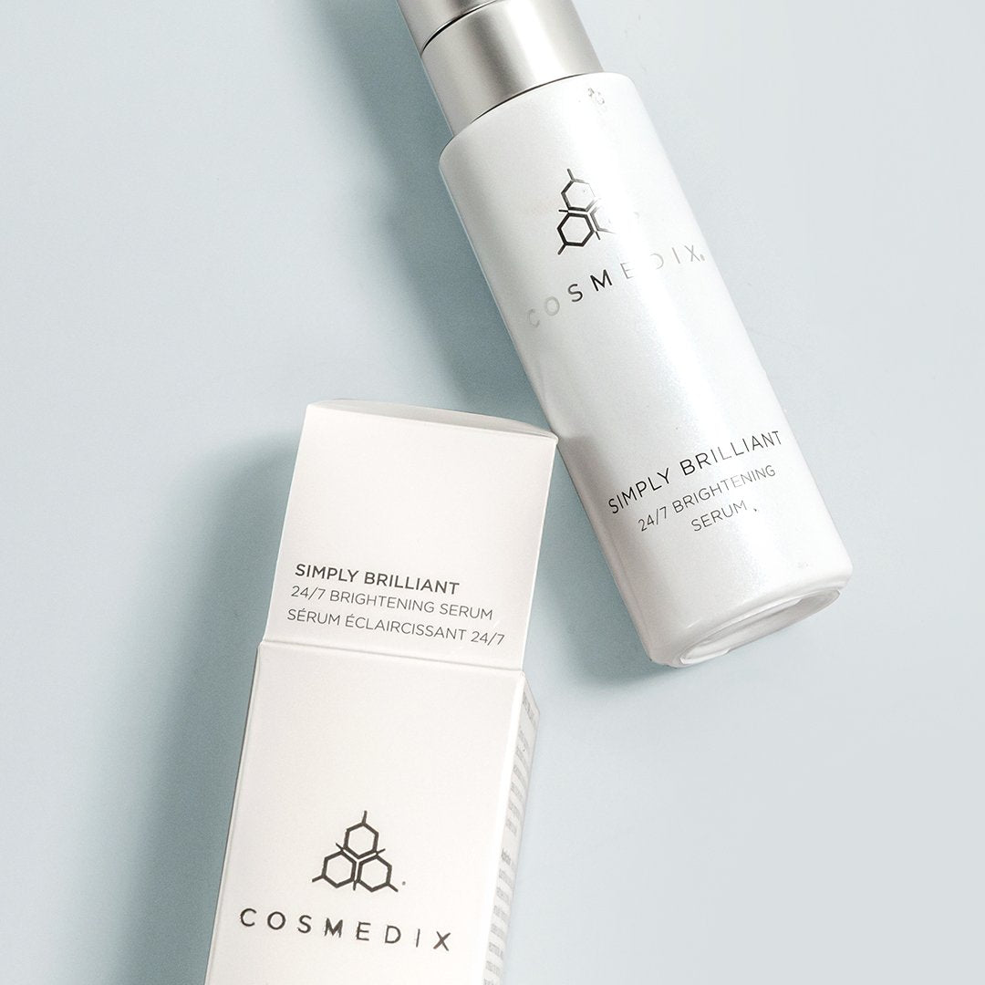 COSMEDIX's Simply Brilliant 24/7 Brightening Serum white product bottle laying down with opened product box against light grey background