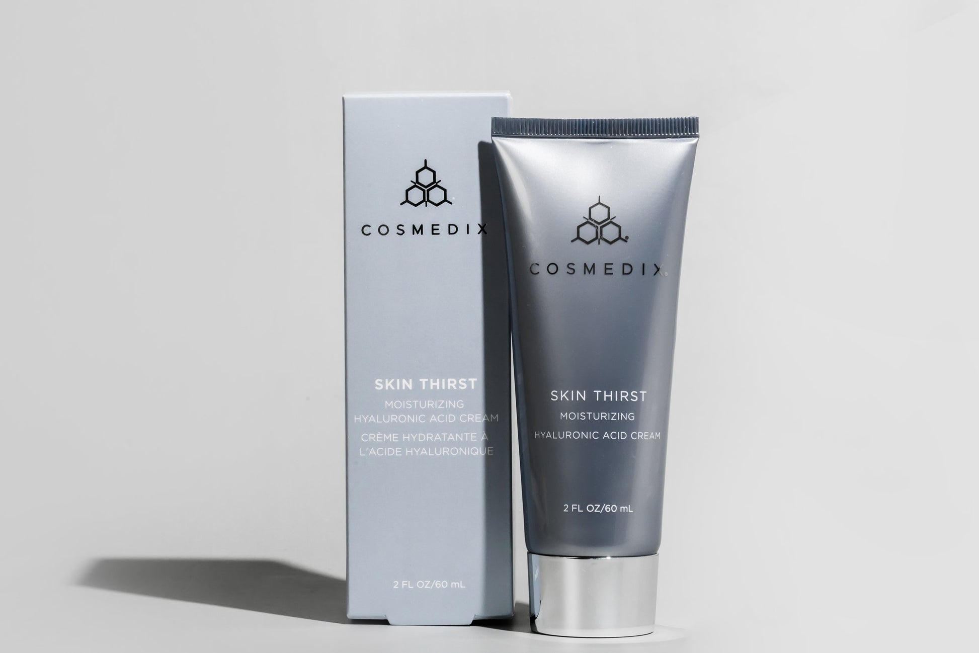 COSMEDIX's Skin Thirst Moisturizing Hyaluronic Acid Cream dark grey product tube standing beside light grey product box against a grey background