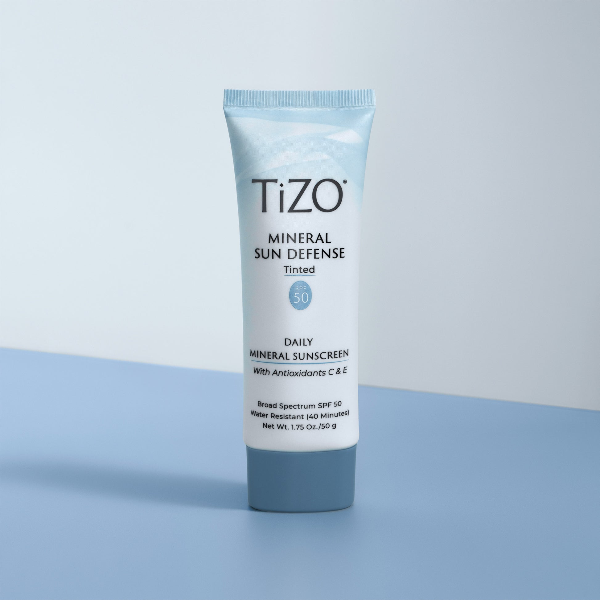 TiZO Mineral Sun Defense Tinted SPF 50 product tube against white and blue background