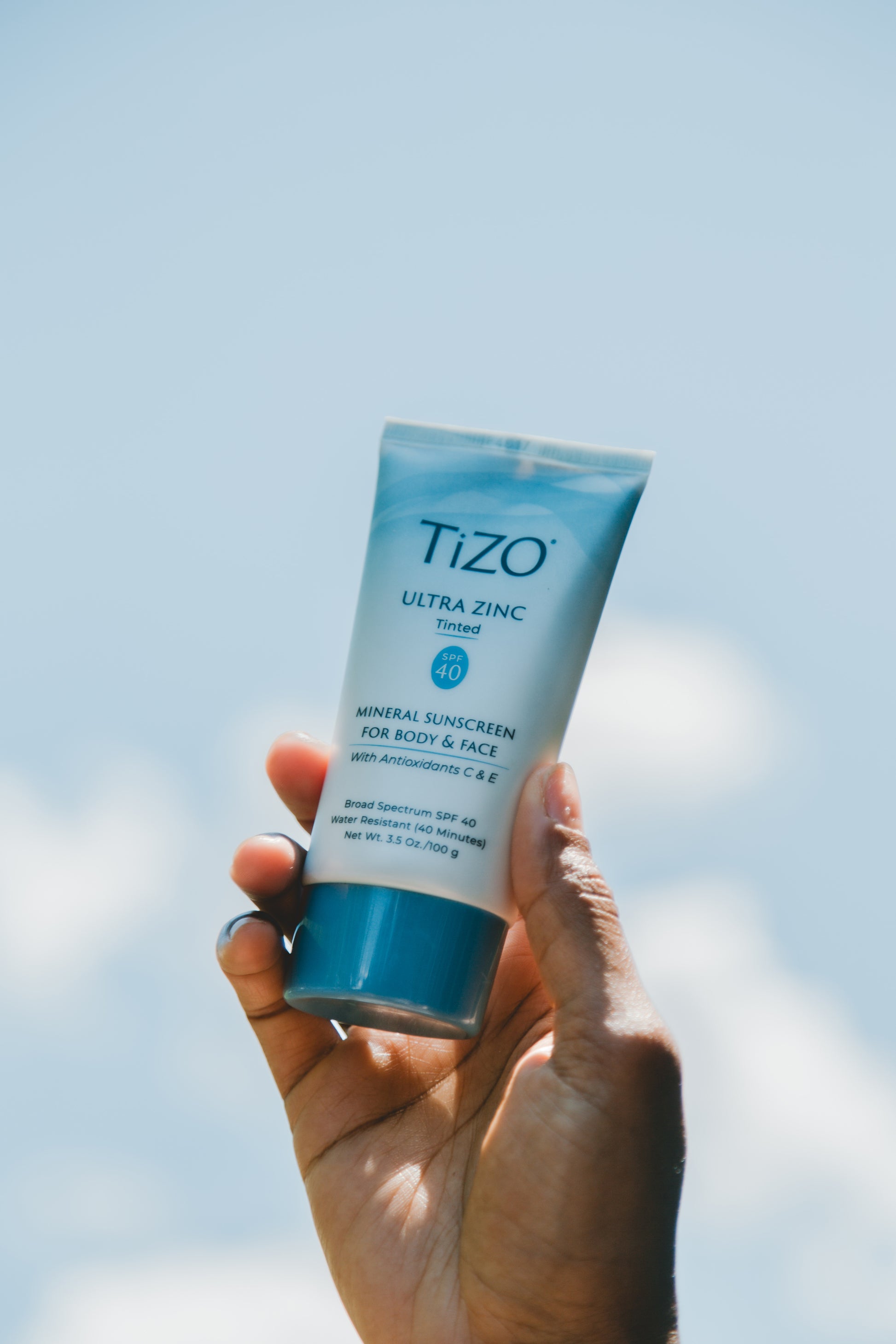 TiZO Ultra Zinc Body & Face - Tinted SPF 40 product tube being held by hand with the sky as the background
