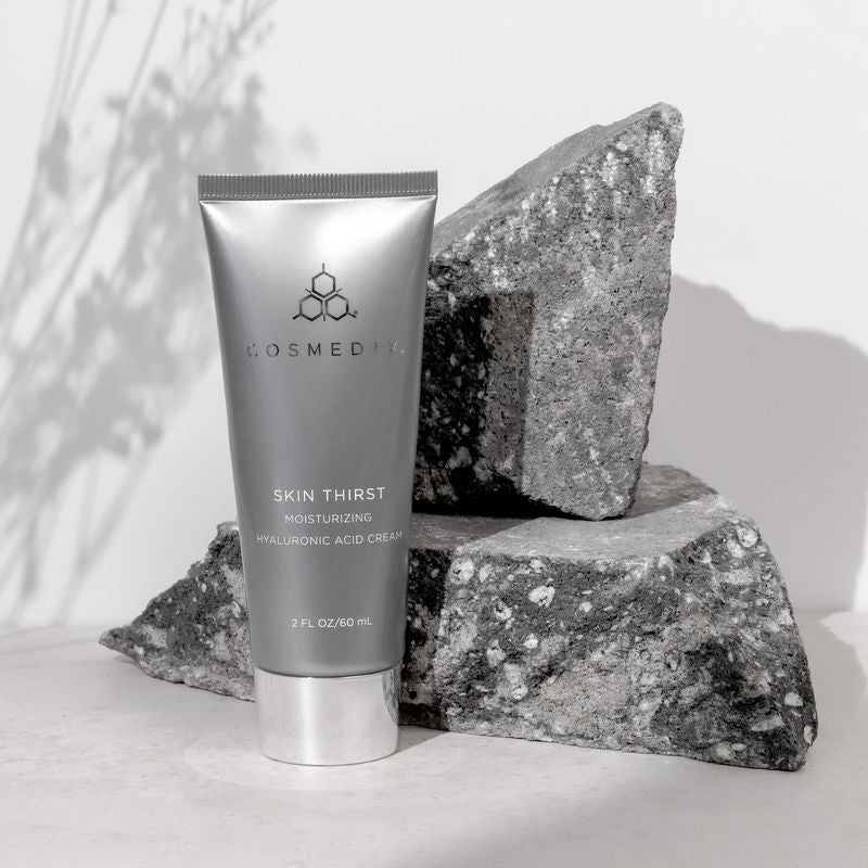 COSMEDIX's Skin Thirst Moisturizing Hyaluronic Acid Cream grey product bottle standing beside granite with light grey background with shadows