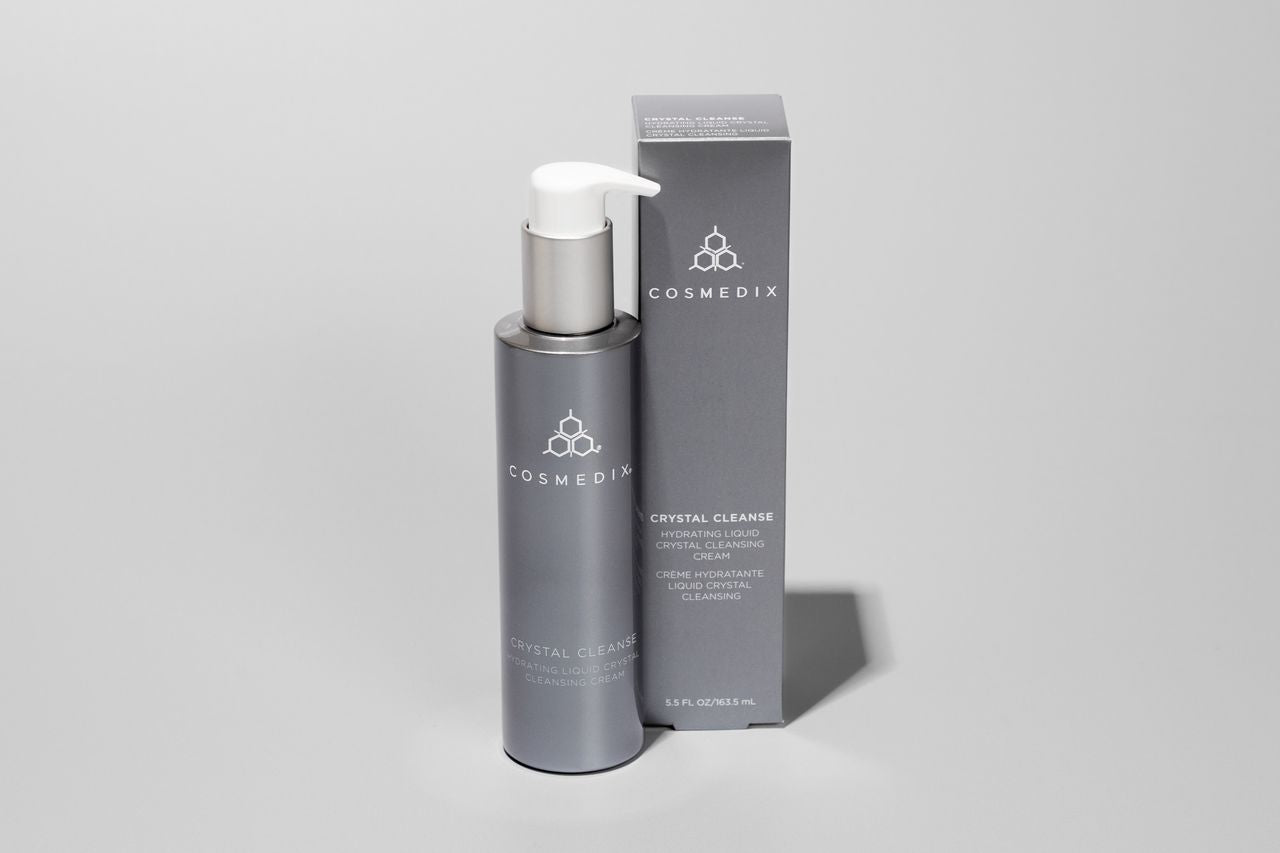 COSMEDIX's Crystal Cleanse in dark grey product bottle with white pump dispenser standing beside dark grey product packaging box and a light grey background.