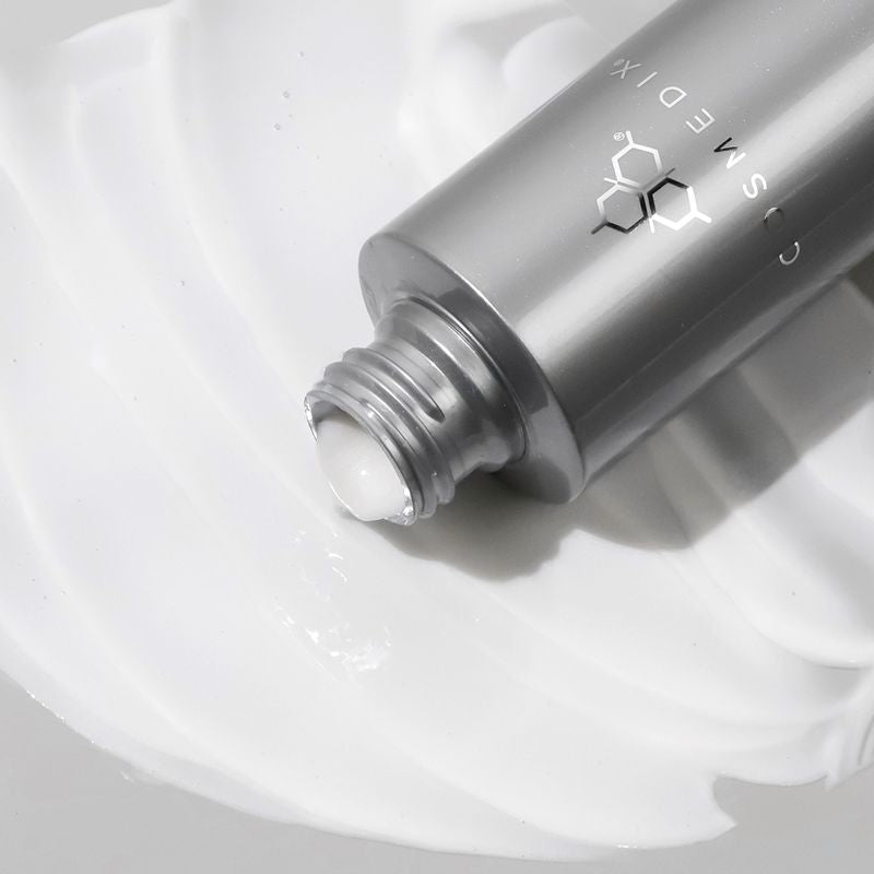 Zoomed in view of COSMEDIX's Crystal Cleanse dark grey product bottle laying on side with cap off and dripping white-colored product
