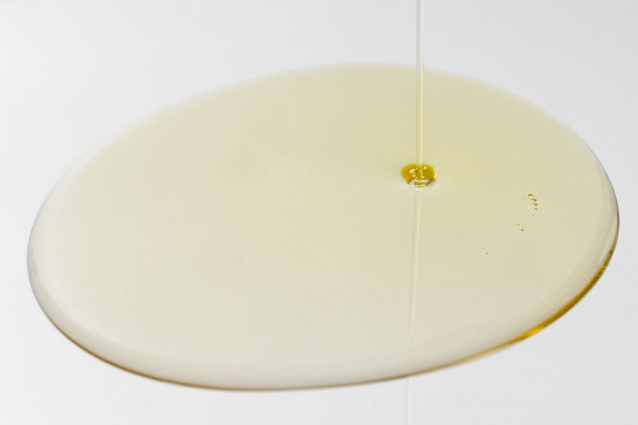 COSMEDIX's Purity Solution Nourishing Cleansing Oil gold colored product droplet against light grey background