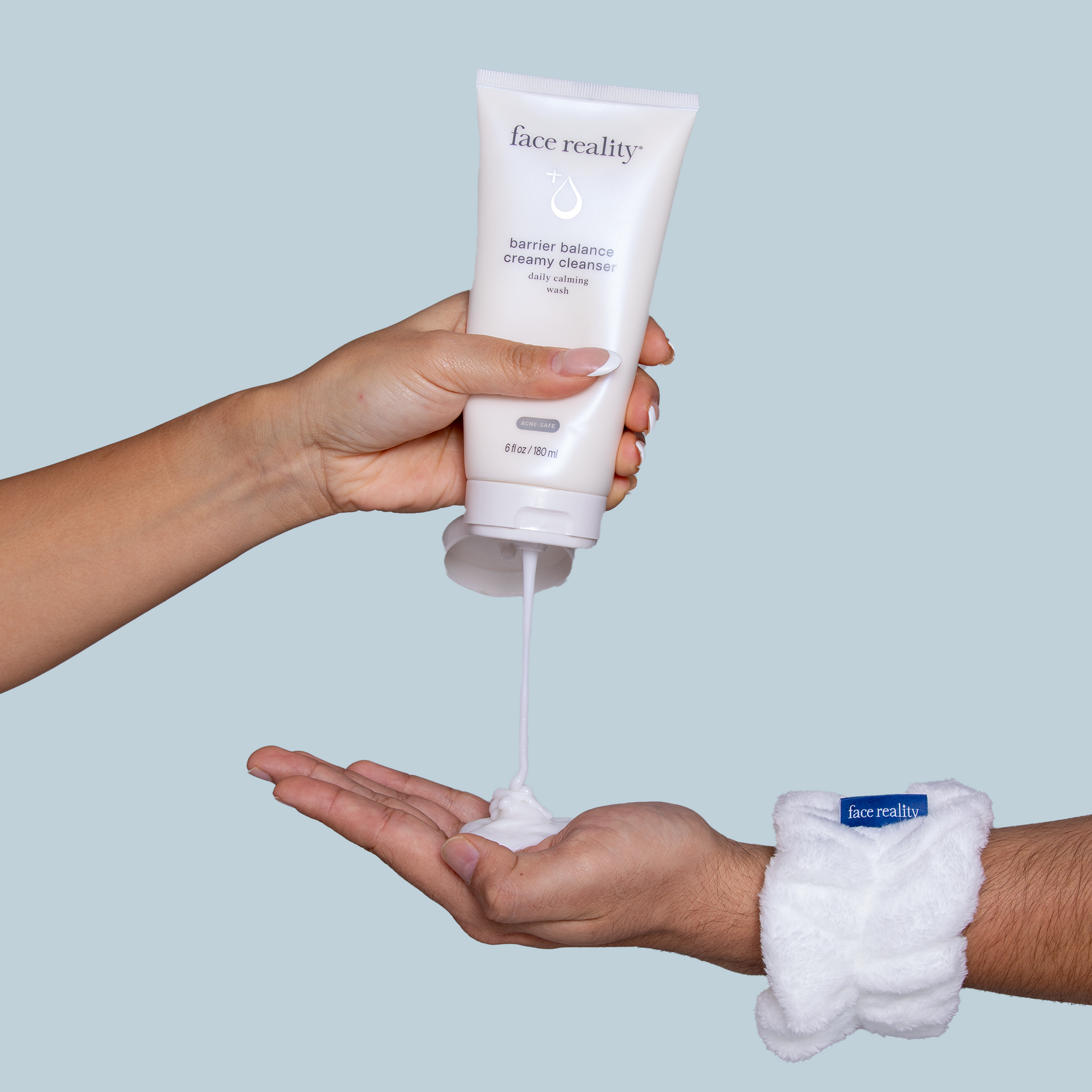 Face Reality's barrier balance creamy cleanser being dispensed by one hand into another hand, with a light blue backdrop