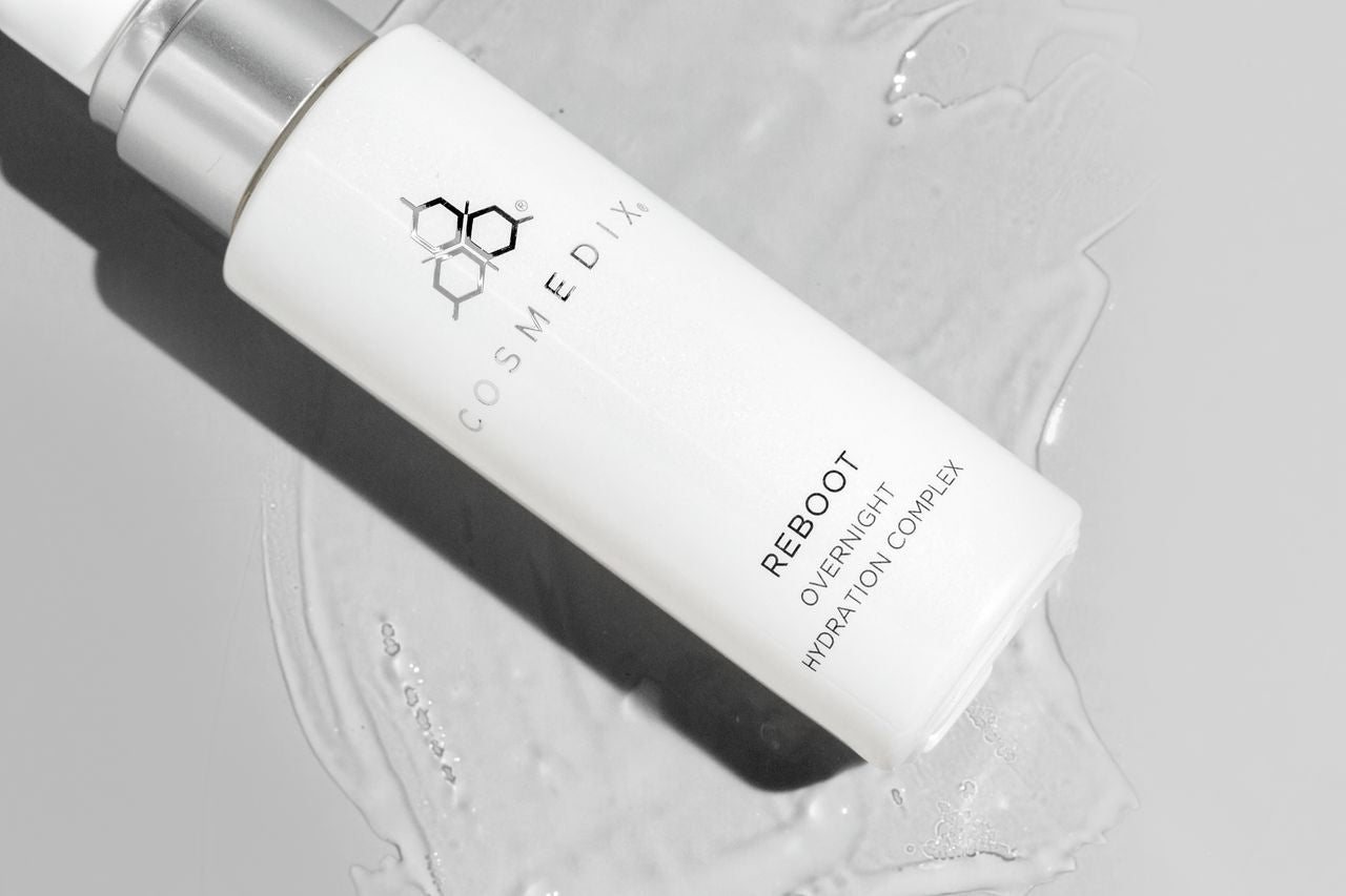COSMEDIX's Reboot Overnight Hydration Complex white colored product bottle laying on clear colored product swatch against a light grey background