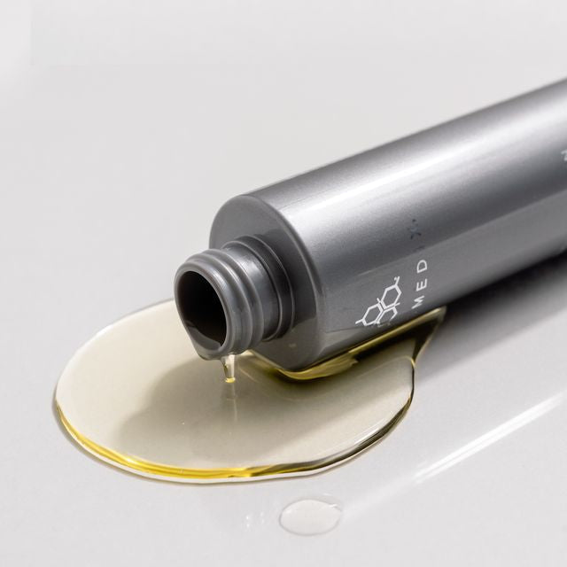 COSMEDIX's Purity Solution Nourishing Cleansing Oil grey product with lid off and dripping gold colored product oil against light grey background