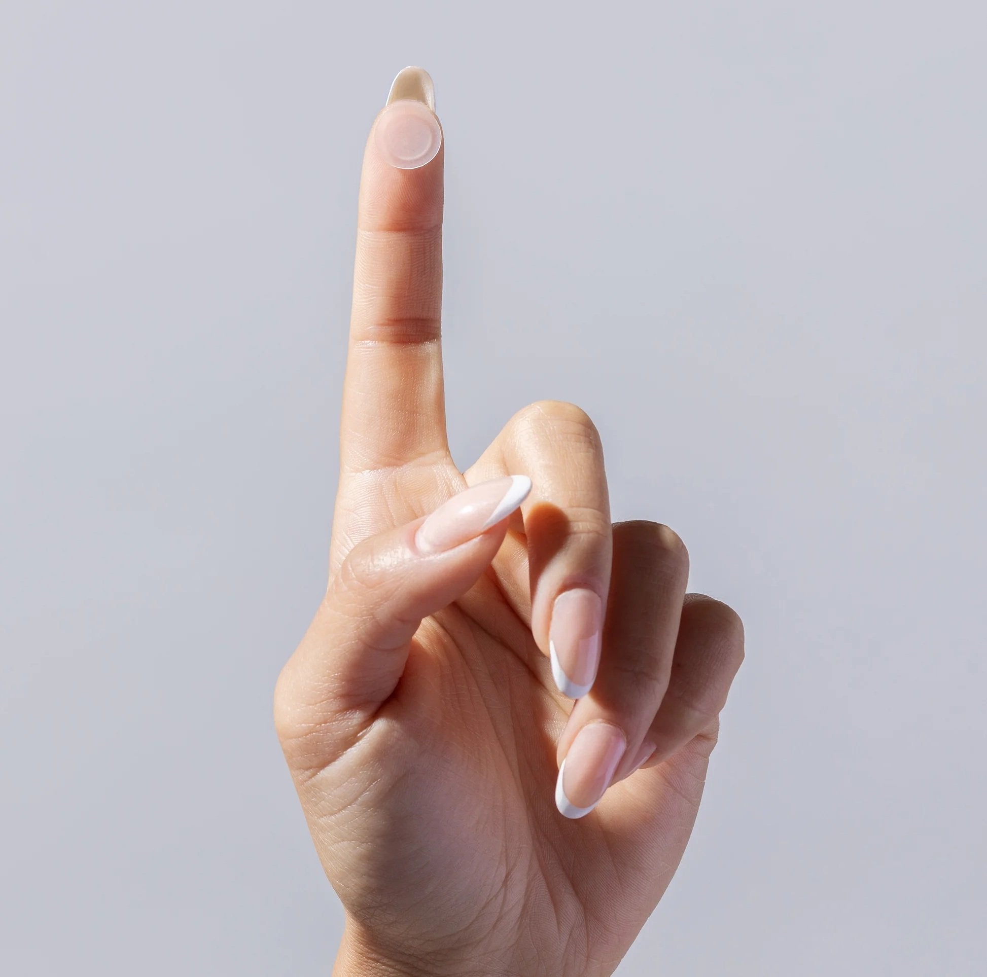 Fingertip with a singular invisiClear hydrocolloid spot patch against a grey background