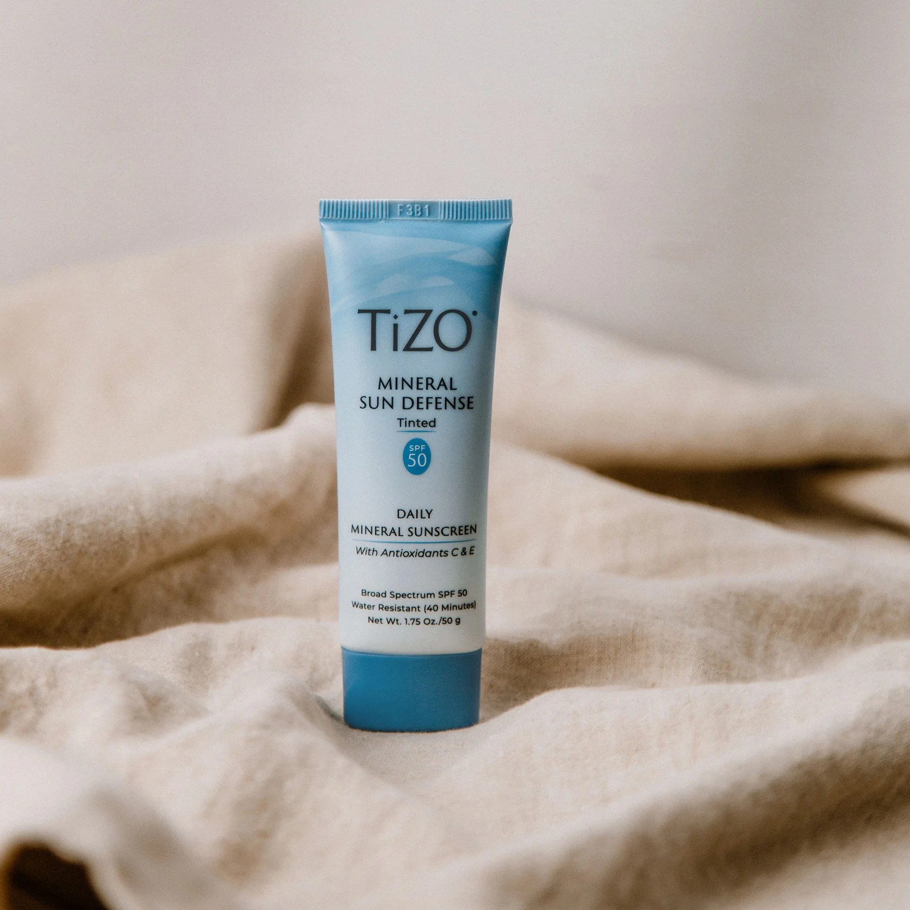 TiZO Mineral Sun Defense Tinted SPF 50 product tube standing on beige cloth
