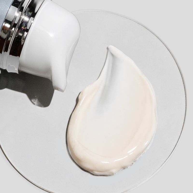 Zoomed in view of COSMEDIX'S Peptide-Rich Defense SPF 50 cream colored product swatch on petri dish and light grey background